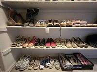Three shelves with multiple pairs of used women's shoes in sizes 9 or larger, including sneakers, boots, flats, and sandals, mostly in neutral colors with some colorful accents.