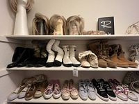 Shelves with multiple pairs of women's shoes and wigs on mannequin heads. Shoes are size 9 or larger, includes black boots, white winter boots, tan boots, sneakers and several wigs.