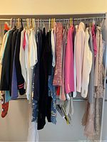 Full view of women's clothing on rack featuring multi-colored tops, dresses, and suit jackets hung on various colored hangers.