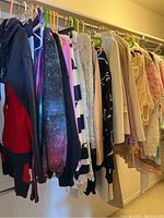 Wide shot of women's clothing hanging on a closet rod showing various sweaters, hoodies, jackets, and tops in different fabrics and colors.