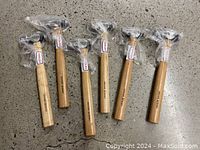 Six Toolex ball peen hammers, all wrapped in plastic on their wooden handles, laid out flat on concrete floor.