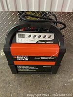 Front view of Black & Decker battery charger showing handle, digital display, control buttons, and brand label.