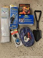 Overview of lot items including booster cables, antifreeze tester, battery charger, folding shovel