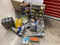 Wide view showing assorted hardware containers, storage drawers, and tools laid out on the floor.