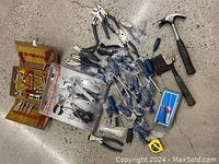 Photo showing several Mastercraft screwdrivers, pliers, two claw hammers, a measuring tape, wrenches, and other assorted hand tools spread out on floor.