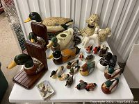 Overview of all duck and dog themed figurines, bookends, and decor items on a white table, showing various sizes and styles of carved wooden ducks, ceramic dogs, and salt and pepper shakers.