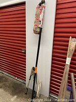 Full view of Fiskars pole lopper and ratchet lopper standing against white panel with red background.