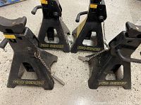 Photo of four black metal Black Jack Pro Series jack stands arranged on a concrete floor, showing the triangular base and safety pin mechanism.