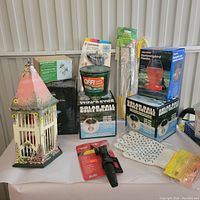 Full view of the lot showing various garden-related items including painted birdhouse, insect repellent, solar balls, hummingbird feeder box, and garden tools.