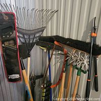 Photo showing a variety of garden rakes, garden hoes, auger tiller, large broom with black bristles, pole pruner and a Job Mate saw in a case.