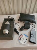 Hand held Niagrassage personal massager with attached wired control, power adapter, black wrist strap, and instructional CD on white surface.