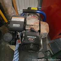 Front view of the Honda GC 160 engine showing black cover and Honda logo with GC 160 branding, mounted on blue frame, with visible signs of rust on metallic parts.