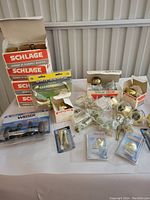 Full view of lot showing boxed Schlage door hardware, loose brass doorknobs, packaging from Weiser and USCAN, and various latch and strike pieces.