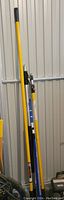 Four multi-extension poles against wall, mostly yellow and blue colors including a Bennett brand adjustable extension pole.