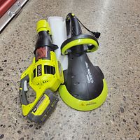 Full shot of two Ryobi garden tools, a Garden Groom Pro and a leaf blower, placed on the floor showing handles and color scheme.