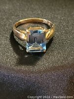 Close-up of ring showing square emerald-cut blue topaz and four-prong setting