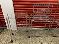 Four stainless steel Metro shelving units shown against a red shutter background. Units include a small 3-tier shelving unit on castors.