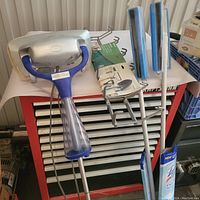 Steam mop unit with blue handle, mop heads with blue cleaning pads and metal attachments on a red tool chest.