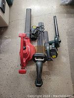 Overview of all three items: large red Toro chainsaw, smaller green Yard Worx chainsaw, and green Yard Worx leaf blower, grouped on floor