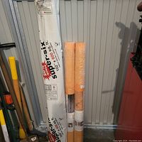 Photo of three rolls standing upright against a wall: one Vapour Supersix vapour barrier and two Schluter-KERDI waterproofing membrane rolls, new in packaging.