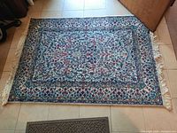 Full view of rectangular wool area rug with floral and geometric designs, showing fringe detailing on one short edge.