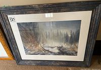 Framed landscape painting showing a misty forest and stream scene with a wood frame