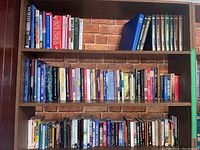 Three-tier bookshelf containing approximately fifty assorted hardcover and paperback books with visible titles covering history, medical references, and novels.