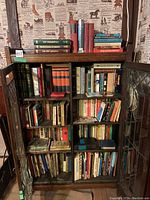 Overview of wooden cabinet with glass doors filled with multiple shelves of assorted books of various sizes, colors, and bindings