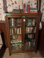 Front view of the wooden bookshelf with glass paneled doors, showing multiple books inside and one broken glass panel.