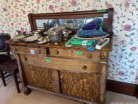 Front view of the wood buffet showing three drawers, two paneled doors, and mirror with items on top.