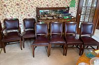 Full view of all six dining chairs near a wooden buffet with items on top, floral wallpaper background