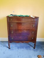 Front view of wood dresser with 4 drawers and round handles showing wear and scratches.