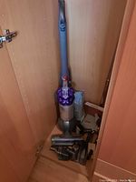 Dyson DC51 upright vacuum cleaner stored in a cabinet, showing full body including handle, cyclone chamber, and floor brush head at base.