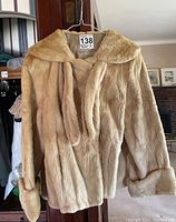 Front view of beige mink fur jacket on hanger showing collar and self-tie detail