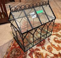 Angled front view showing the rectangular glass case with black metal frame and hinged roof lid.