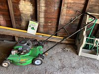 Full view of green Lawn-Boy 21 Silver Series mower with attached handlebar and owner's manual leaning against the wall.
