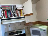 Microwave and overhead cabinet with multiple cookbooks visible.