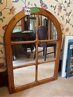 Full view of the arched wall mirror leaning against a floral wallpapered wall, showing its wooden frame and reflective glass panes.
