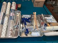 Overview of painting and wallpaper supplies, showing metal trays, caulking applicator, brushes, and wallpaper rolls
