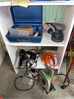 Five power tools including drill, jig saw, skill saw, orange drill and black sander on white shelves.