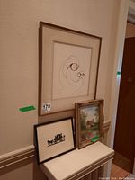 Three framed artworks against wall: large abstract print, smaller silhouette print, and small landscape painting