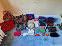 Full overview of all purses, bags, wallets and coin wallets arranged on floor including fabric and leather-like materials.