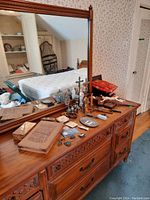 Wide view of wooden dresser with mirror showing various metal religious items including crosses, crucifix statues, medallions, displayed alongside two books stacked on the dresser.