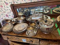 Photo showing the collection of silver plated tea set and serving platters on wooden surface in front of mirror