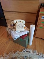 Vintage rotary dial telephone on top of papers and a green metal cabinet with wooden front panels