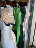Vintage women's clothing including various dresses and a bright lime green Gino Charles jacket hanging on a rack showing multiple garments close together