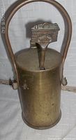 Front view of the brass fire starter can with decorative lid handle resembling a fireplace and shovel.