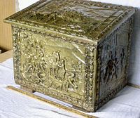 Front corner view showing a detailed horse and human embossed scene on the copper surface with decorative border trim and aged patina.