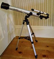 Full view of the Edu Science Astrolon refractor telescope mounted on aluminum tripod indoors on wooden floor near wall and door.