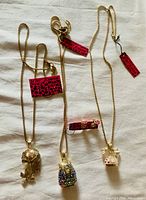 Three gold-tone necklaces with large pendants and pink rotary telephone earrings displayed on a white background.